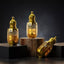 Three gold perfume bottles labeled 'Oud Wood', 'White Oud', and 'Baccarat Rouge' with decorative elements on a light background.