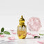 Gold perfume bottle labeled 'Versace Pink' with flowers, fruits, and spices on a white background