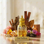Gold bottle labeled 'Oud Saffron' surrounded by flowers, spices, and decorative elements on a reflective surface.